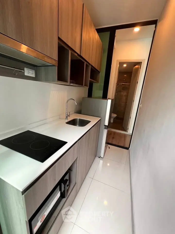 Modern compact kitchen with sleek cabinetry and electric cooktop in stylish apartment.