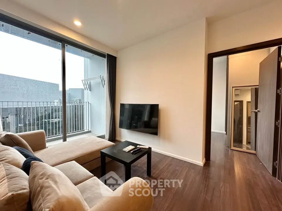 Modern living room with cozy sofa and wall-mounted TV, featuring a large window with balcony view.
