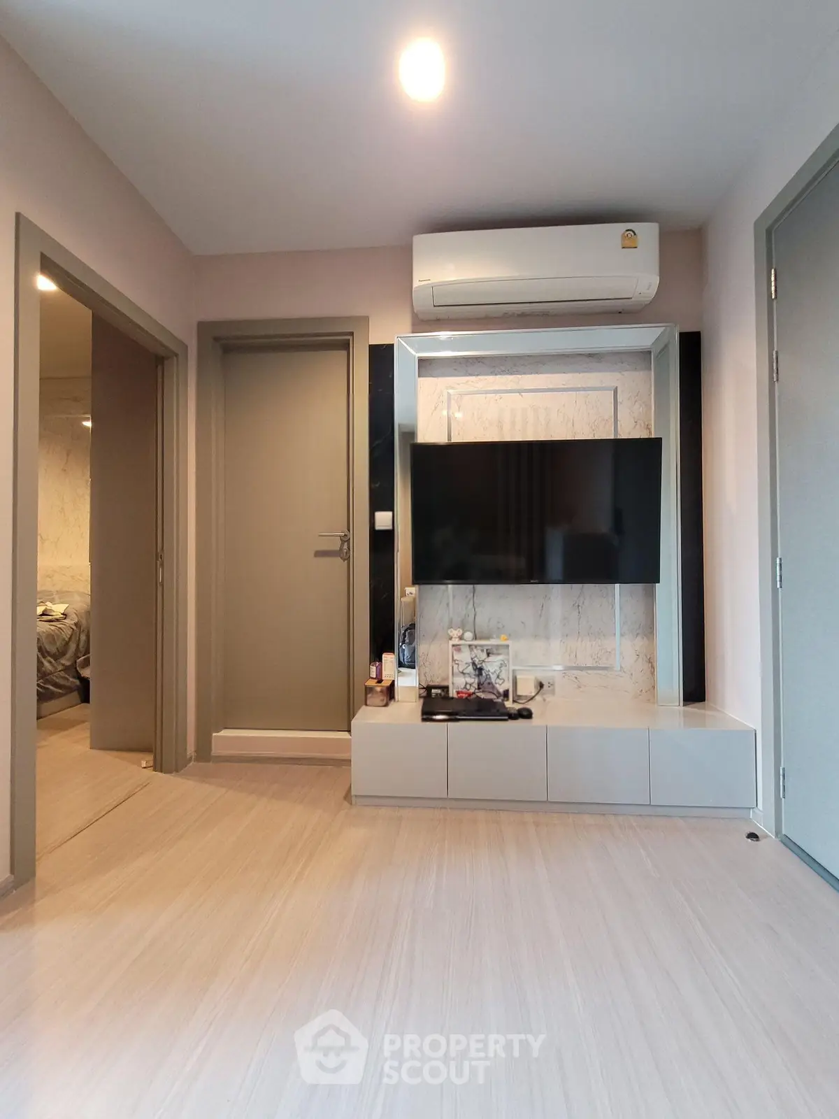 Modern living room with sleek TV setup and air conditioning, featuring light wood flooring and neutral tones.