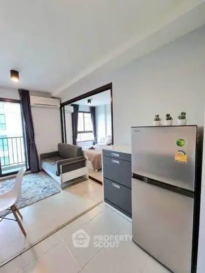 Modern apartment interior with open layout, featuring a cozy living area and sleek kitchen with stainless steel fridge.