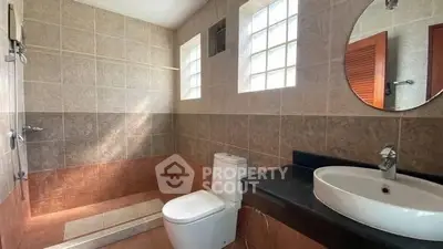 Modern bathroom with tiled walls, round mirror, and natural light.
