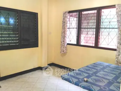 Cozy bedroom with tiled floor and large windows, featuring a simple bed setup and floral curtains.