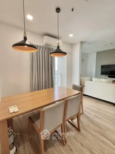 Modern dining area with wooden table and stylish pendant lights in open-plan living space.