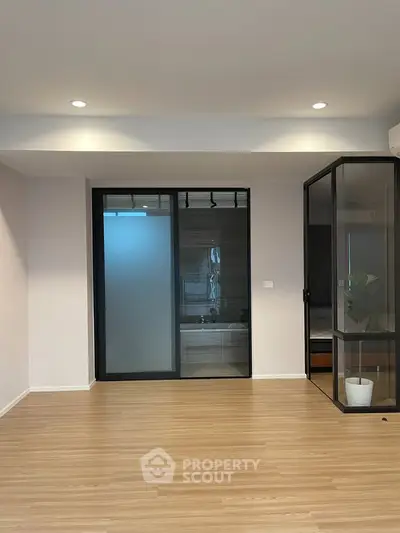 Spacious modern living room with wooden flooring and glass doors, perfect for contemporary living.