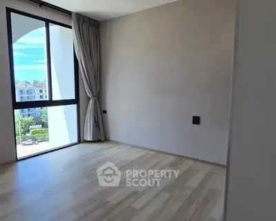 Spacious empty room with large window and wooden flooring, offering natural light and scenic view.