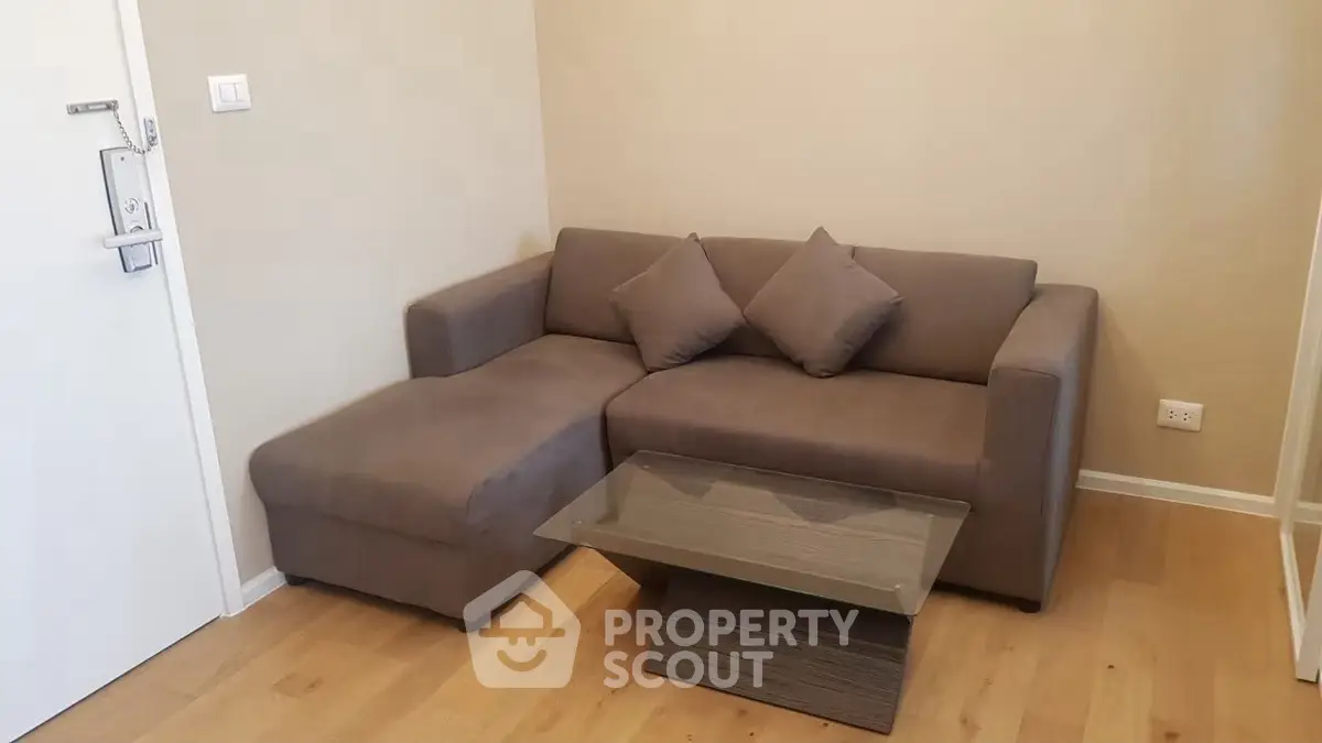 Cozy living room with modern gray sofa and glass coffee table on wooden flooring.