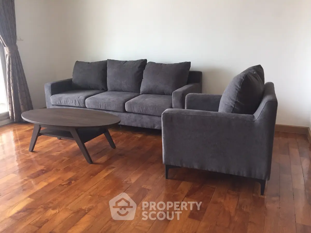 Spacious living room with modern gray sofa and wooden coffee table on polished hardwood floor.
