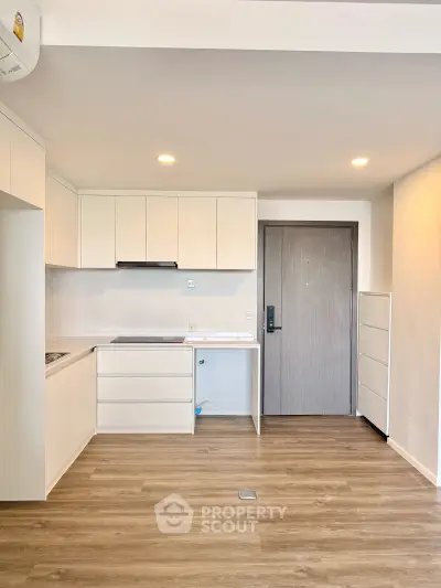 Modern minimalist kitchen with sleek cabinetry and wood flooring in a compact apartment.