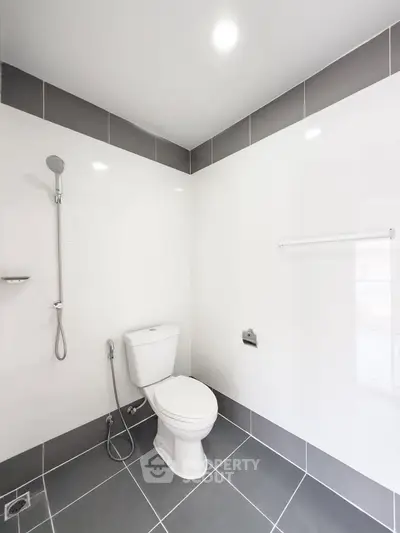 Modern bathroom with sleek gray and white tiles, featuring a toilet and shower area.
