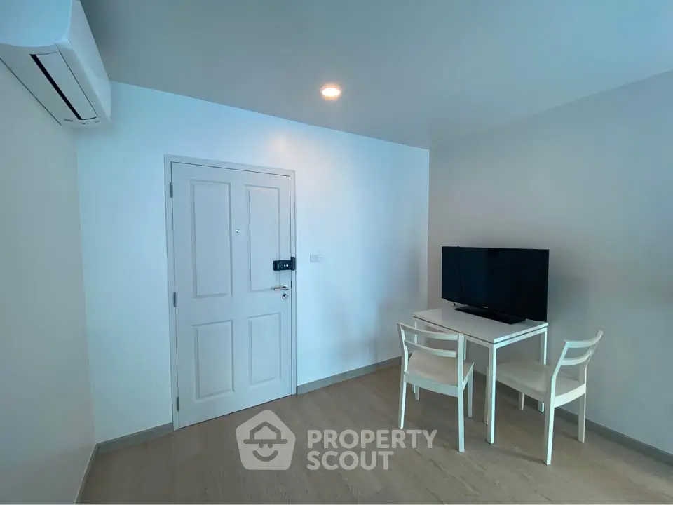 Modern minimalist living room with TV and dining set, featuring sleek white furniture and air conditioning.