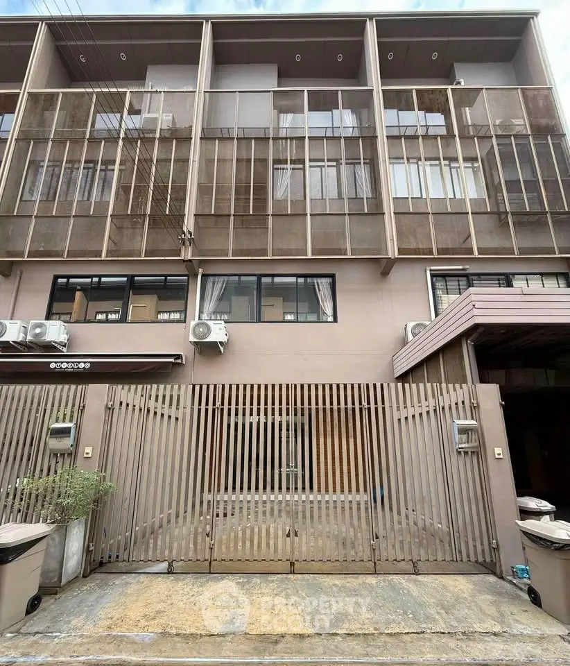 Modern townhouse exterior with gated entrance and multiple air conditioning units.