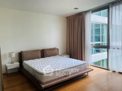 Spacious bedroom with large window and modern furnishings in a high-rise apartment.