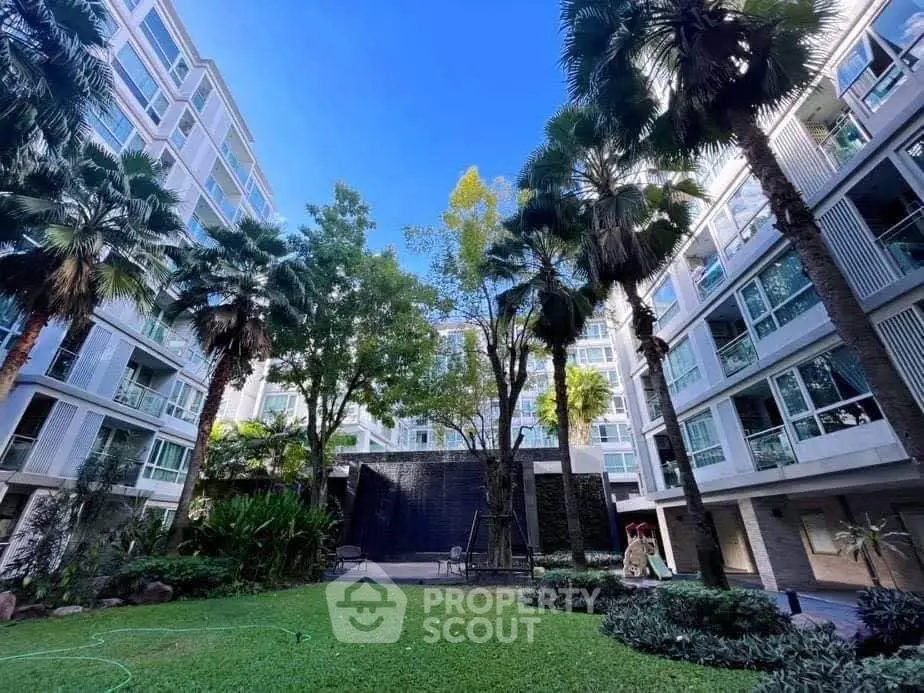 Modern apartment building with lush garden and tall palm trees under a clear blue sky.