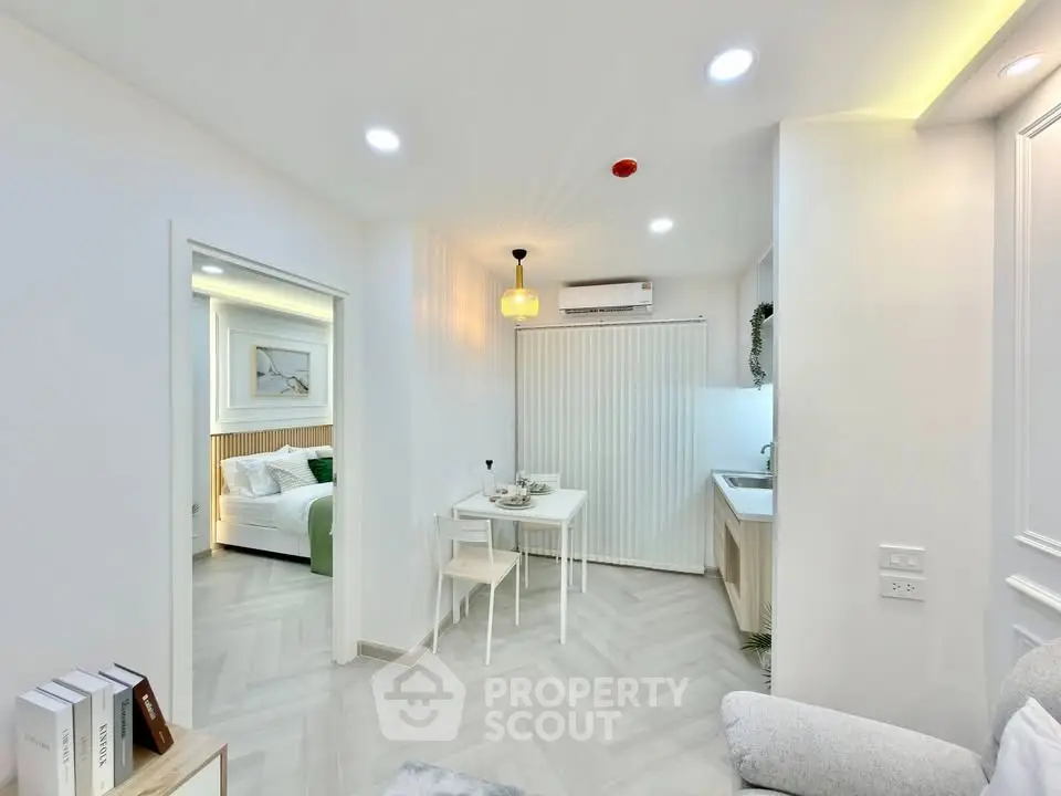 Modern open-plan living room with dining area and view into a cozy bedroom, featuring elegant decor and bright lighting.