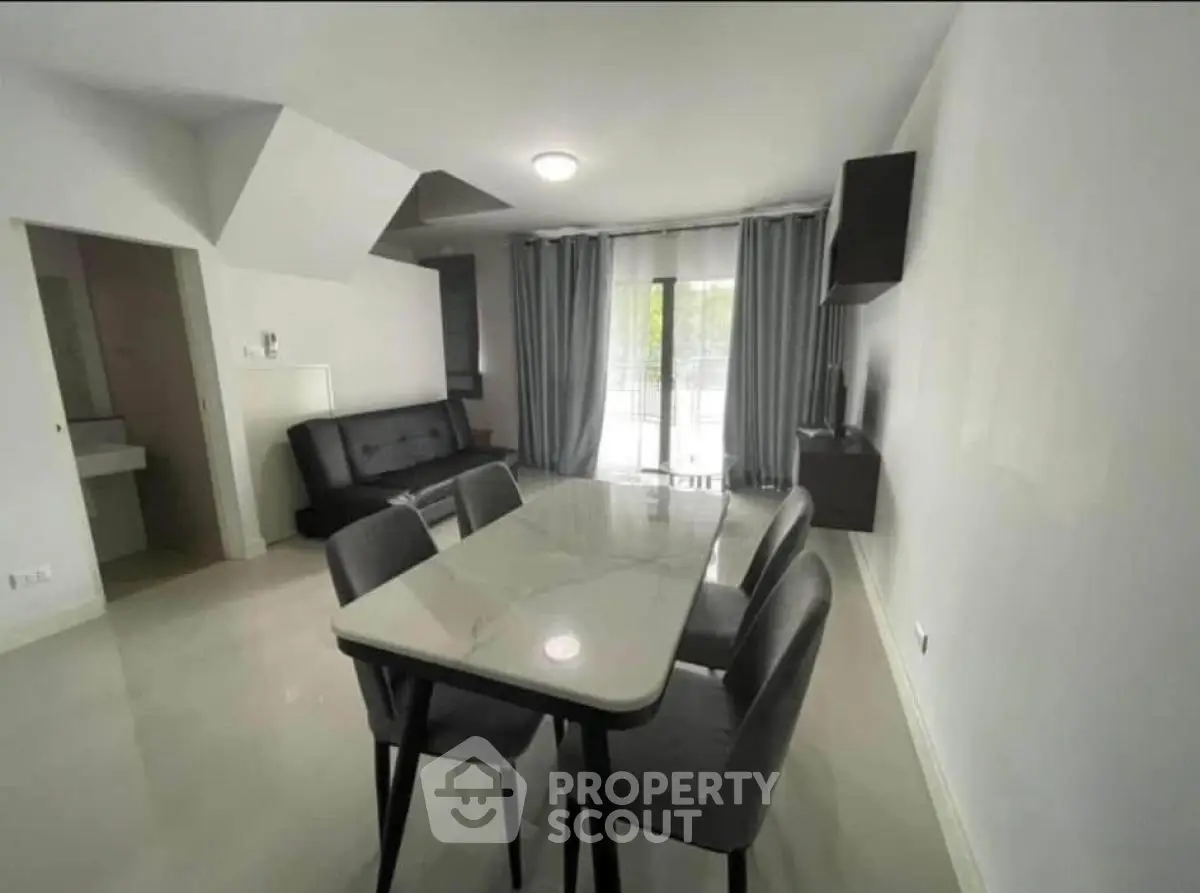 Modern dining area with sleek table and chairs, adjacent to a cozy living space with natural light.