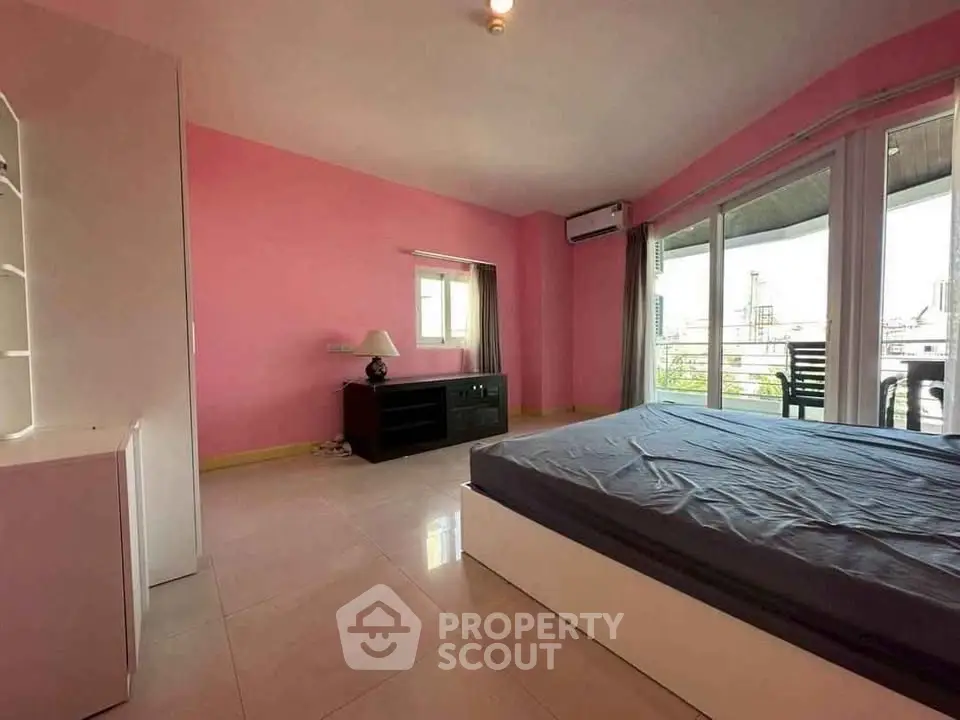 Spacious bedroom with balcony access and pink walls, featuring modern furnishings and ample natural light.