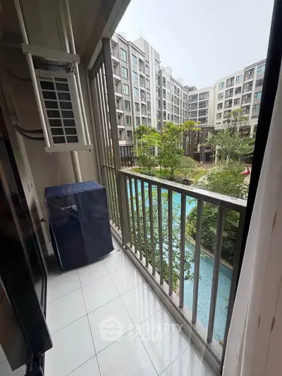 Charming balcony view overlooking modern apartment complex with lush greenery and pool.