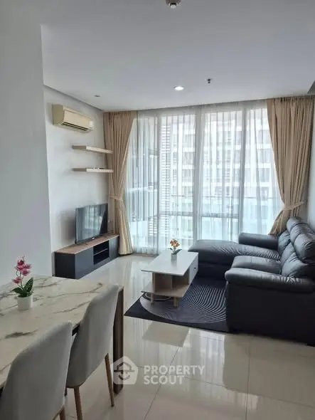 Modern living room with large windows, sleek furniture, and natural light in a high-rise apartment.