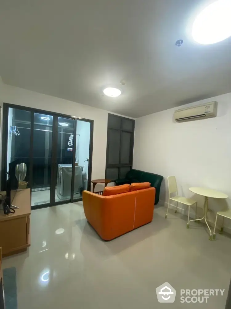 Modern living room with vibrant orange sofa and sleek glass doors leading to balcony