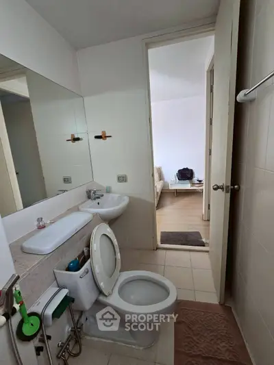 Modern bathroom with white fixtures and view into a cozy living room.
