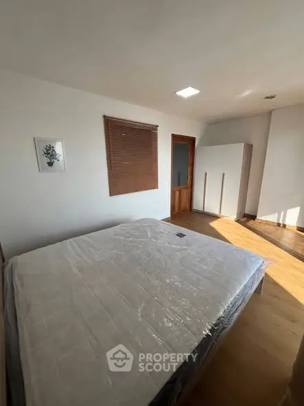 Spacious bedroom with natural light and wooden flooring, featuring a large bed and wardrobe.