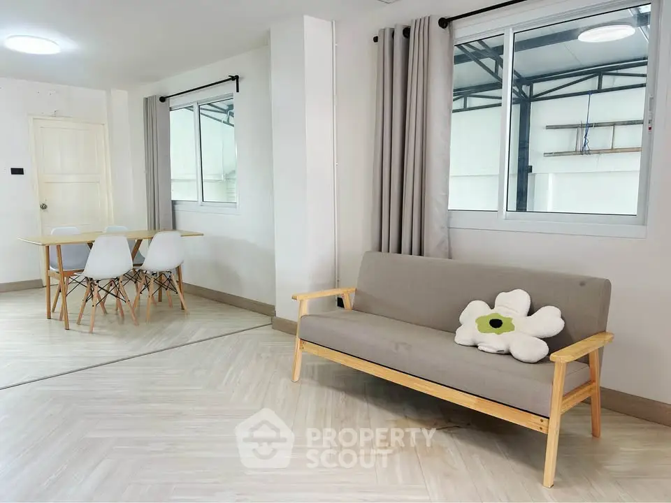 Modern living room with minimalist decor, featuring a cozy sofa and dining area with natural light.