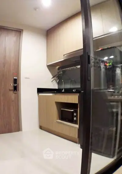 Modern compact kitchen with sleek cabinetry and built-in microwave in a stylish apartment.