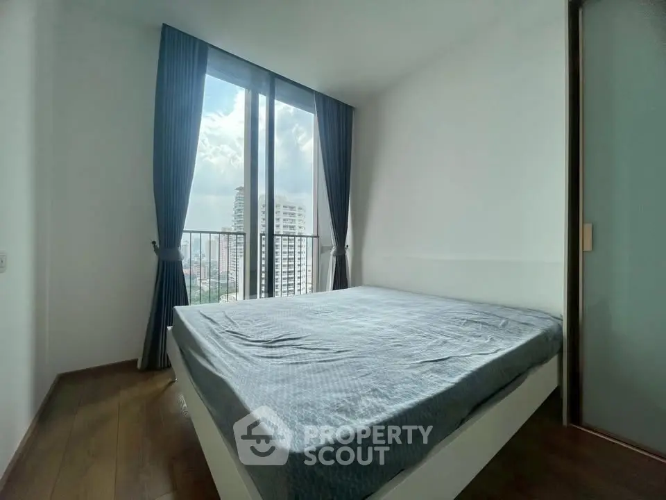 Bright bedroom with large window offering stunning city view in modern apartment.