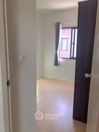 Cozy empty bedroom with wooden flooring and window view, ready for personalization.