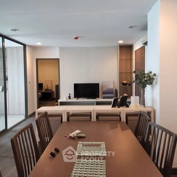 Modern dining area with wooden table and chairs, open layout to living room with TV and decor.
