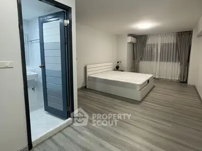 Spacious bedroom with modern flooring and attached bathroom in a stylish apartment.