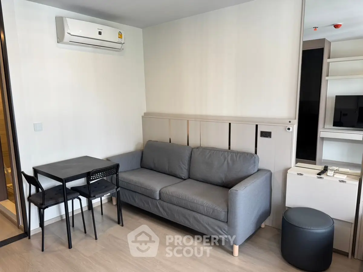 Modern living room with gray sofa, dining table, and air conditioning in a stylish apartment.