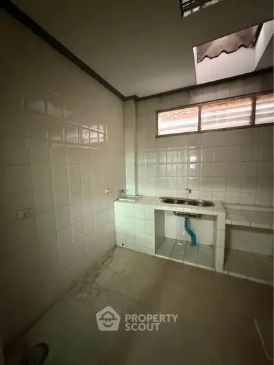 Spacious tiled kitchen with dual sink and natural light, ideal for renovation.