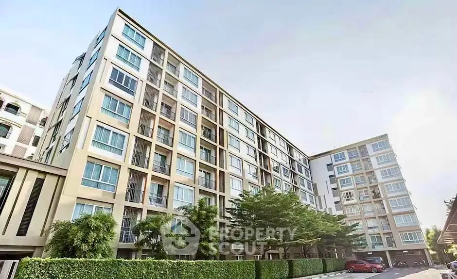 Modern multi-story residential building with lush greenery and parked cars.