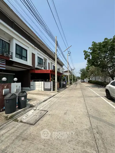 Modern townhouse exterior on a quiet residential street with clear skies and lush greenery.