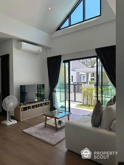 Modern living room with high ceiling and large windows opening to a garden view.