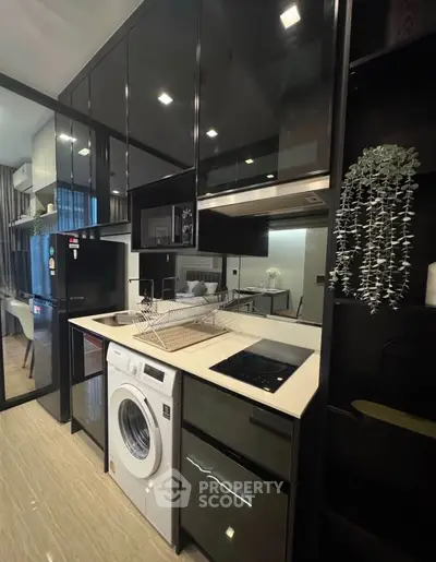 Modern kitchen with sleek black cabinets, washing machine, and electric stove in a compact layout.