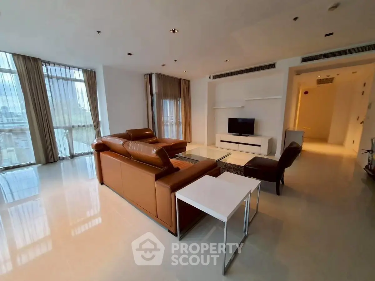 Spacious modern living room with leather sofa and large windows offering city views.