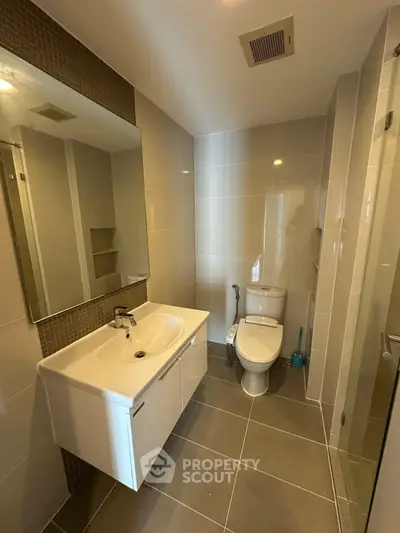 Modern bathroom with sleek fixtures and neutral tiles, featuring a spacious vanity and toilet.