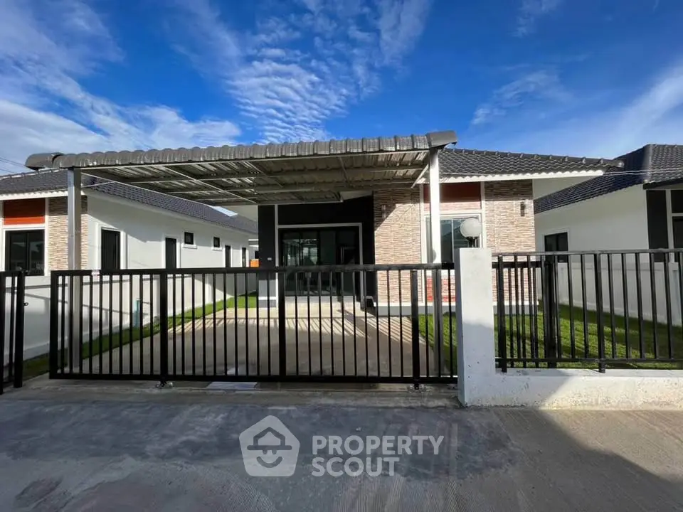 Modern single-story house with gated driveway and stylish facade under a clear blue sky.
