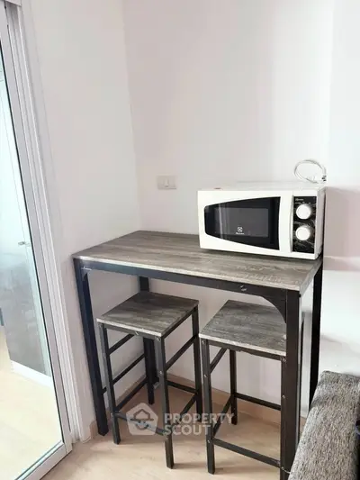 Compact kitchen corner with microwave and bar stools in modern apartment.