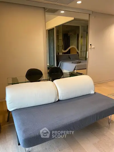 Modern living room with stylish sofa and glass table, reflecting a cozy bedroom in the mirror.