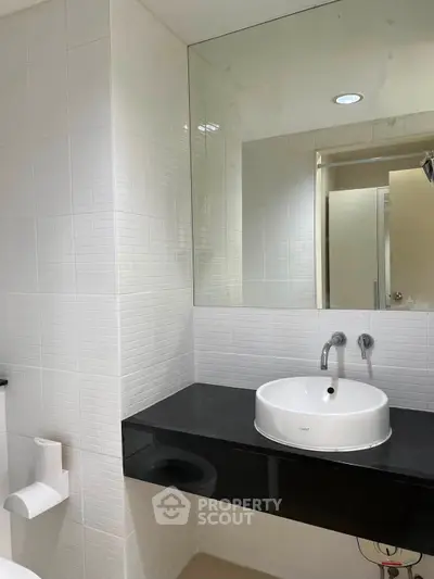 Modern bathroom with sleek black countertop and white basin, featuring minimalist design and wall-mounted faucet.