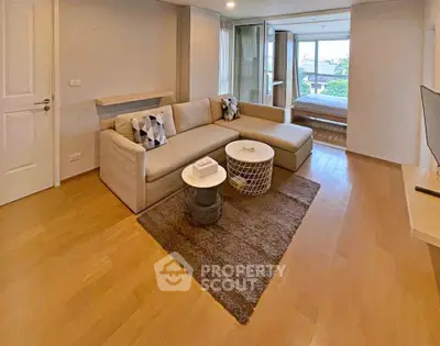 Spacious modern living room with cozy sectional sofa and wooden flooring, leading to a bright bedroom.