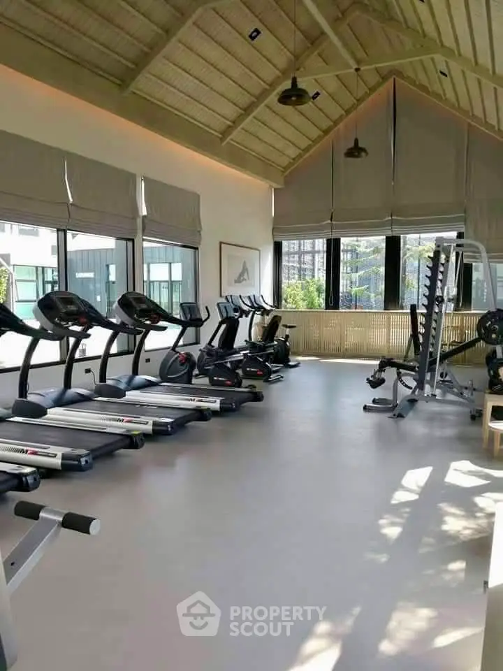 Spacious gym with modern equipment and large windows offering natural light and city views.