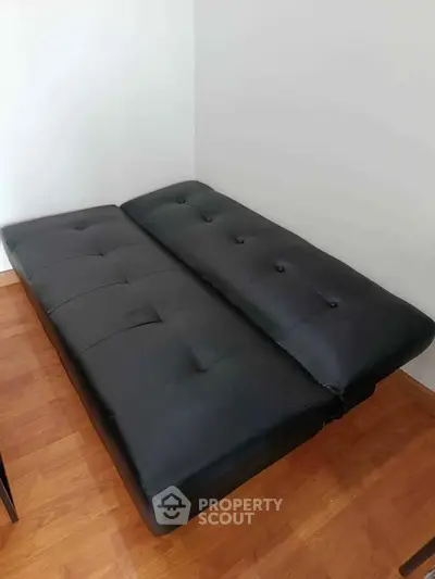 Modern black futon bed in a minimalist room with wooden flooring.