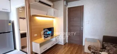 Modern living room with wooden flooring, compact TV unit, and adjacent kitchen area in cozy apartment.