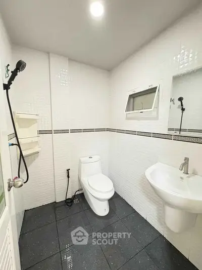 Modern bathroom with sleek fixtures and white tiled walls, featuring a toilet and sink.