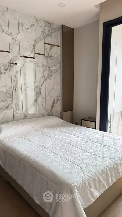 Modern bedroom with marble accent wall and cozy bed in stylish apartment.