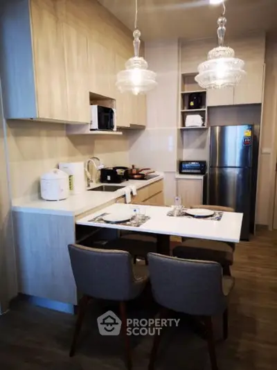 Modern kitchen with sleek cabinetry and dining area, featuring stylish lighting and stainless steel appliances.